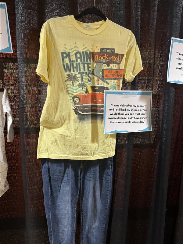 Example outfit for the what were you wearing exhibit. Blue Jeans with Yellow Tshirt. Accompanied by a sign which states survivor's experience.